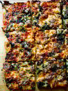 Just-baked grandma-style pizza, cut into squares on a cutting board.