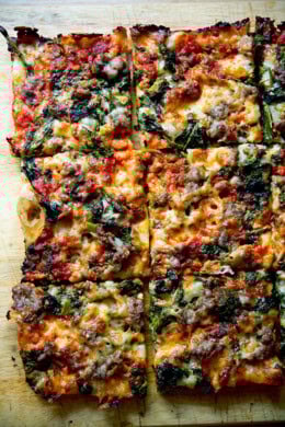 Just-baked grandma-style pizza, cut into squares on a cutting board.