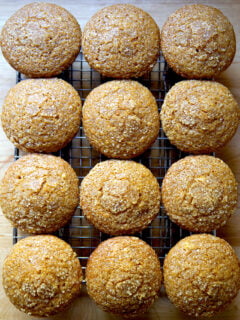 Twelve just-baked pumpkin muffins on a cooling rack.
