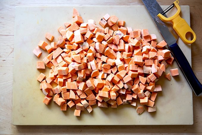 Cubed sweet potatoes on a cutting board aside a chefs knife and peeler. - 31