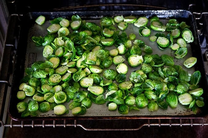 A hot sheet pan filled with halved Brussels sprouts seasoned with olive oil and salt.