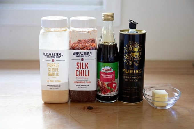 A few seasonings on a countertop: garlic powder, silk chili, pomegranate molasses, olive oil, and butter.