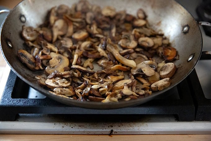 A large pan on the stovetop filled with browned mushrooms for turkey tetrazzini. - 42