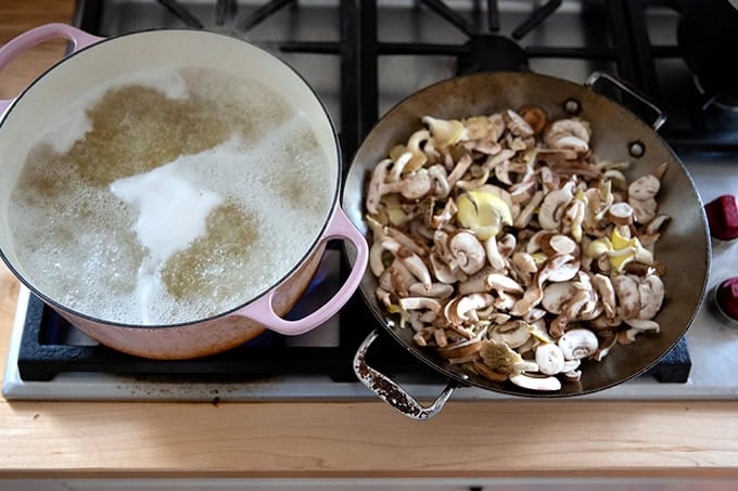 A large pot on the stovetop boiling pasta aside a large sauté pan filled with mushrooms.  - 40