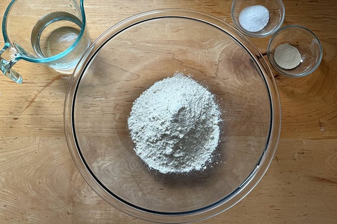 The ingredients to make a giant overnight sandwich roll on a countertop: flour, water, salt, yeast.