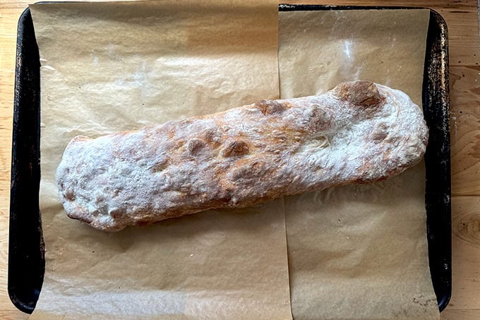 Just-baked giant sandwich roll on a parchment-lined sheet pan.