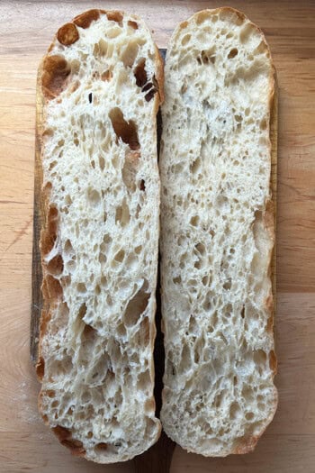 Giant sandwich roll dough, halved on a cutting board.