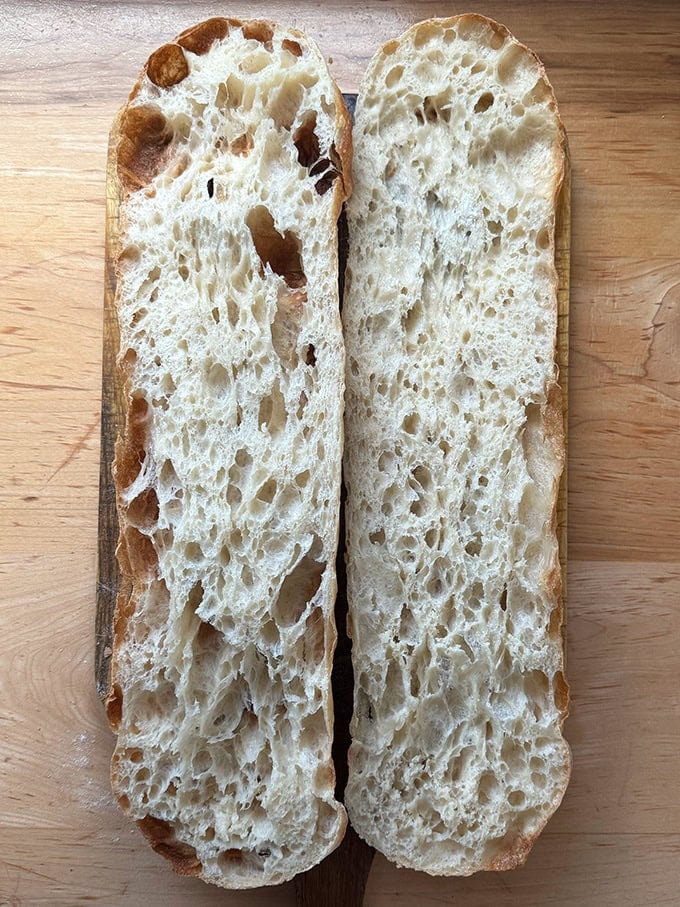 Giant sandwich roll dough, halved on a cutting board.