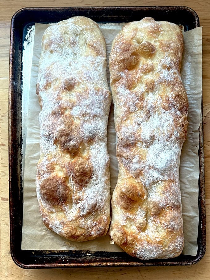 Two overnight sandwich rolls, just baked on a parchment-lined sheet pan.