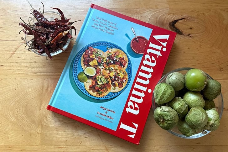 A cookbook, Vitamina T, aside a bowl of tomatillos and chiles de arbol.