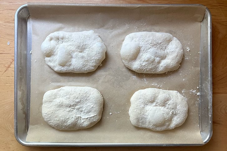 Four overnight sandwich rolls unbaked on a sheet pan.