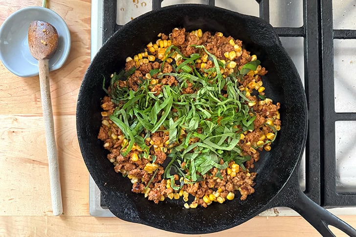 Basil added to a skillet holding chorizo and corn.