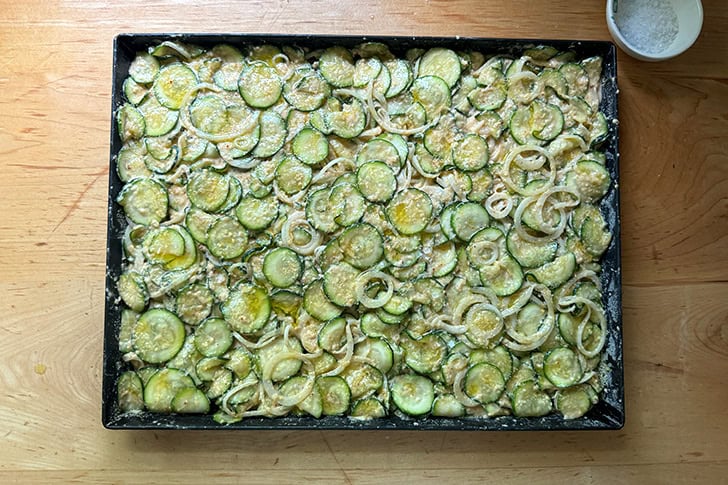 An unbaked sheet pan of Scarpaccia brushed with olive oil and sprinkled with sea salt — ready for the oven.