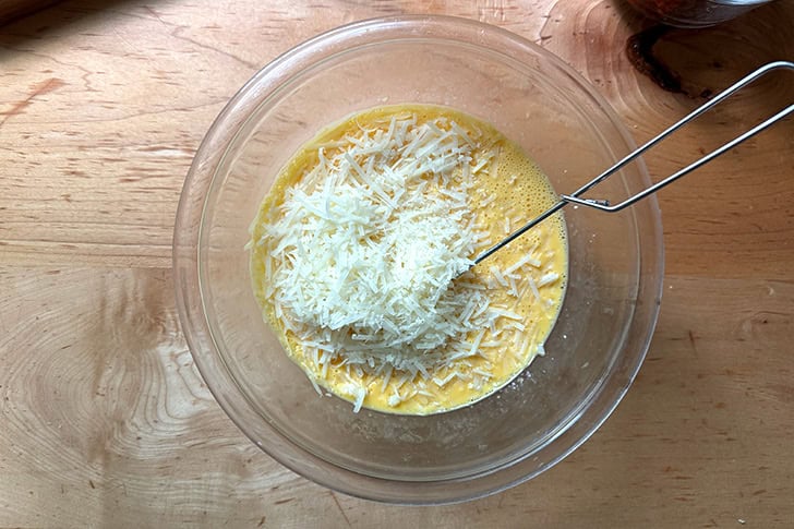 A bowl of whisked eggs, heavy cream, salt, and grated Manchego cheese.