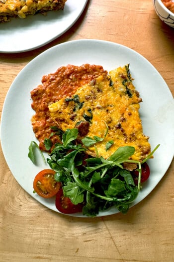 A plate of frittata atop a smear of romesco aside a small salad.