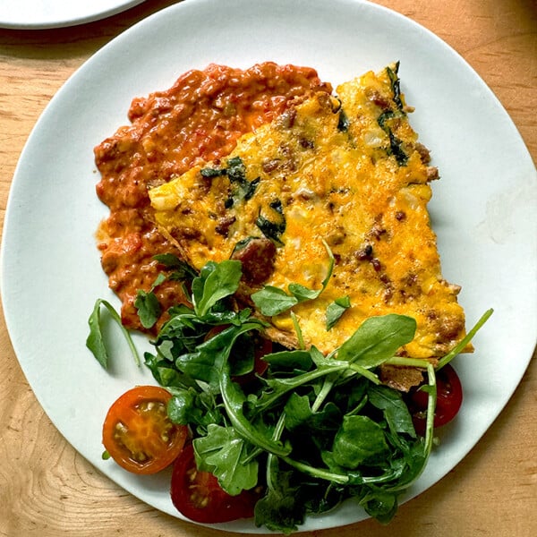 A plate of frittata atop a smear of romesco aside a small salad.