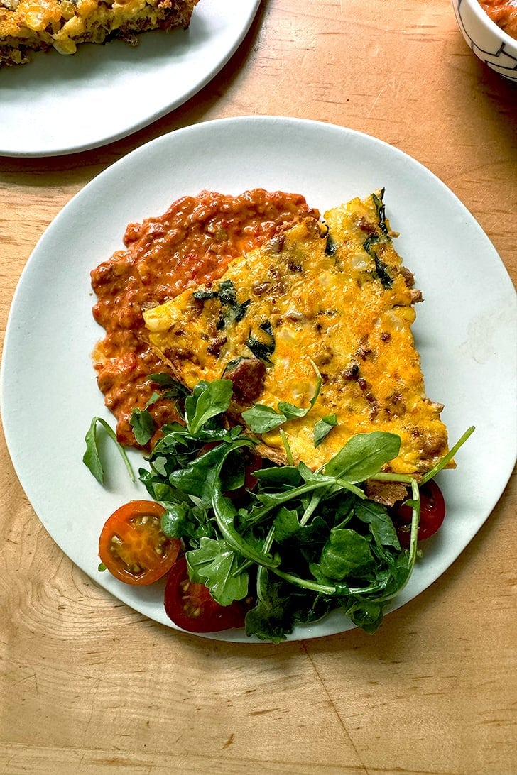 A plate of frittata atop a smear of romesco aside a small salad.