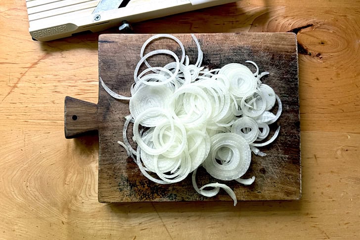 A cutting board topped with thinly sliced onions.