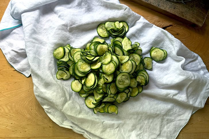 A flour sack towel filled with salted and squeezed zucchini slices.
